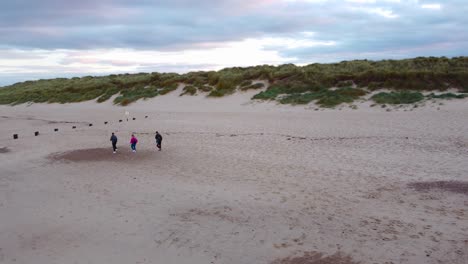 aerial shot orbiting around a family walking along a beach, revealing the beautiful coastline at horsey gap on a cold winter's day norfolk, england, uk