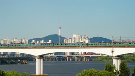 a subway trains travel across the dangsan railway bridge in both directions over the hangang river, with the iconic namsan tower and the sprawling cityscape of seoul, south korea, in the background