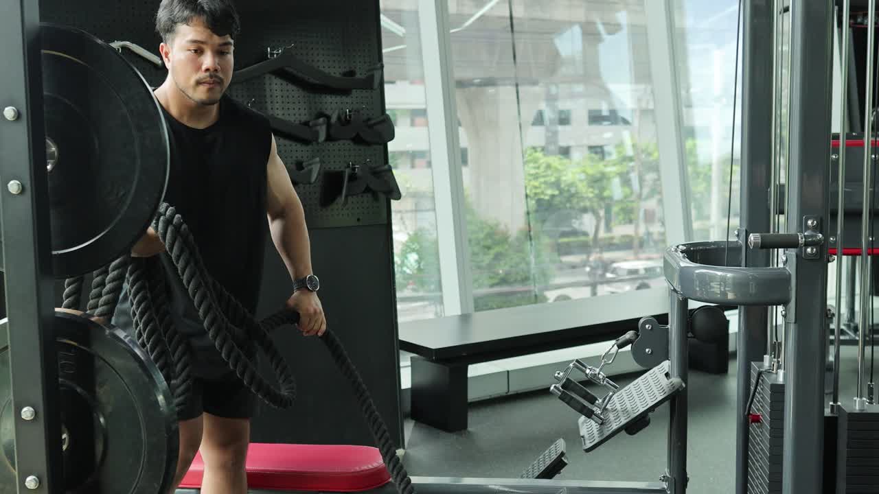 A man tidies tricep ropes in a well-lit gym, emphasizing organization and fitness routine