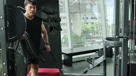 a man tidies tricep ropes in a well-lit gym, emphasizing organization and fitness routine