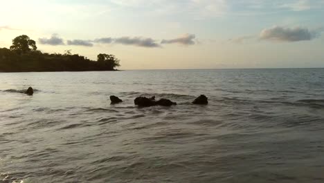 Aerial-towards-rocks-on-water-sunset-beach,-São-Tomé-Island