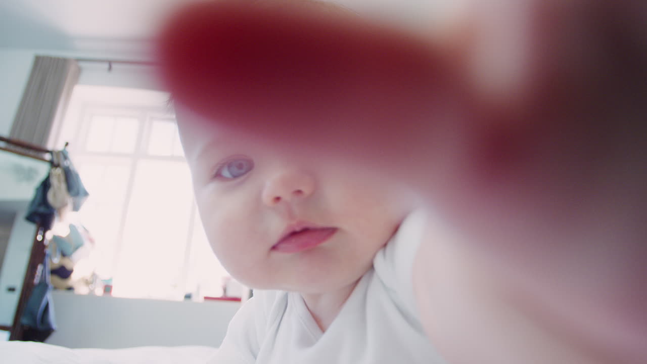 부모 의 침대 에 앉아 있는 아기 소년 이 카메라 를 향해 손 을  ⁇ 고 있다