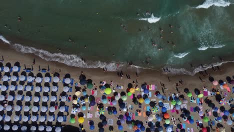 Vista-De-Pájaro-De-La-Gente-En-Una-Playa-Concurrida-En-Verano-Con-Sombrillas-Y-El-Mar