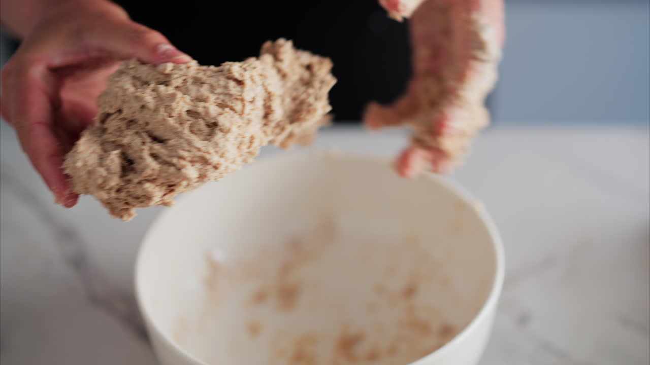Close up of a woman's hands kneading dough in a white bowl