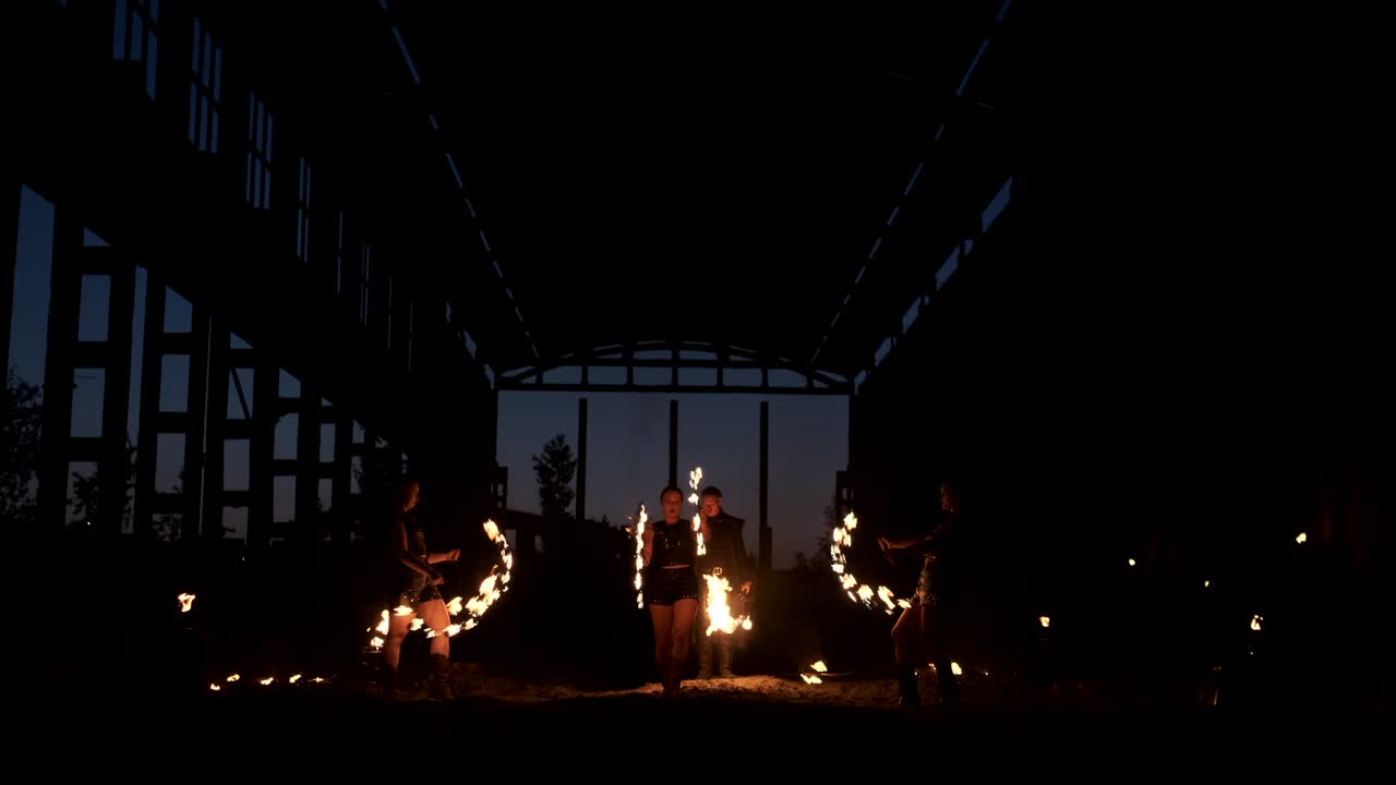 A group of people with fire and torches dancing at sunset in the hangar in slow motion. Fire show