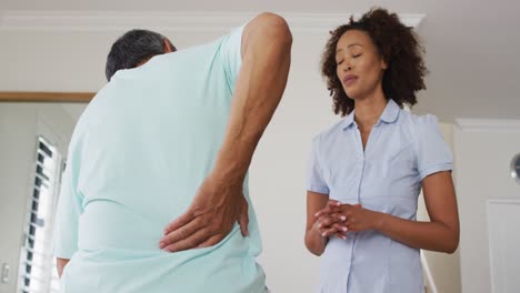 Mixed-race-female-physiotherapist-talking-to-senior-man-holding-his-back