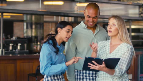 Equipo-De-Personal-Multicultural-Que-Trabaja-En-Un-Restaurante-O-Cafetería-Mirando-Una-Tableta-Digital.