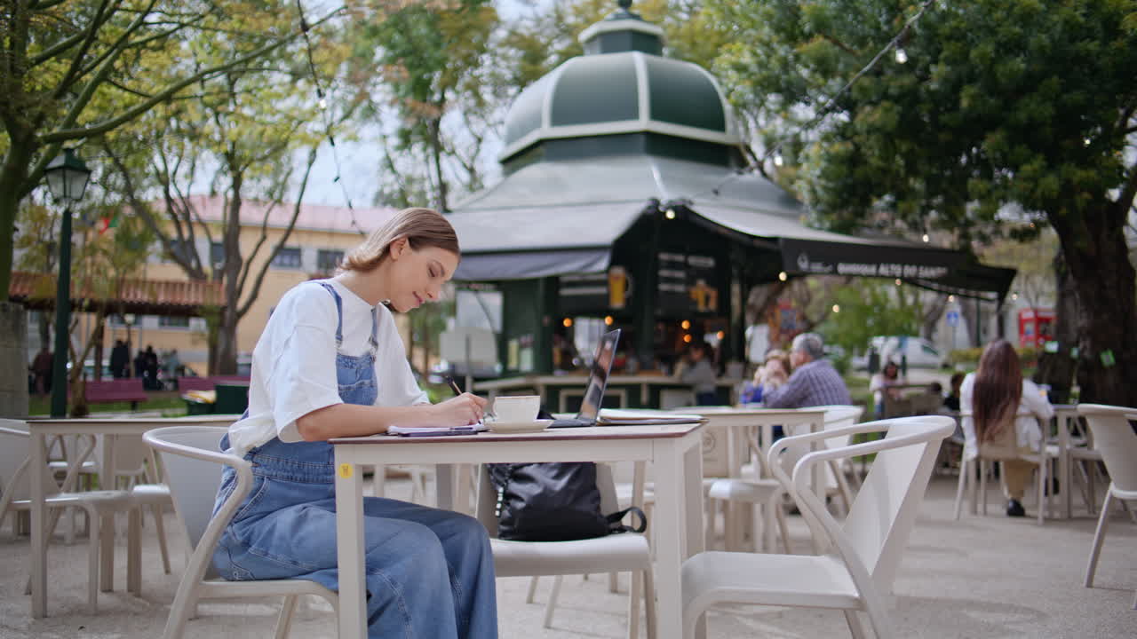 Carefree woman writing cafe outdoors. Relaxed female student working at laptop