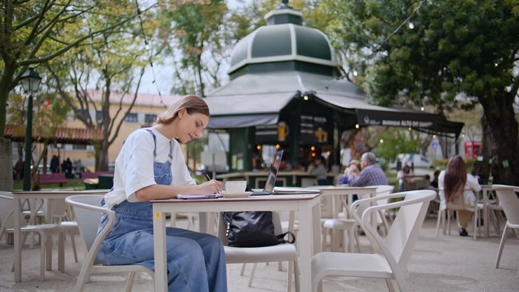 Carefree woman writing cafe outdoors. Relaxed female student working at laptop