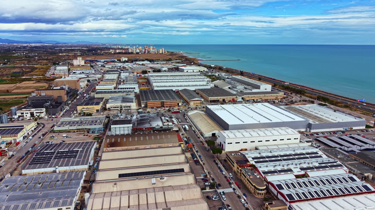 Industrial area near coastline showing warehouses and ocean in a clear sky with scattered clouds during daytime hours