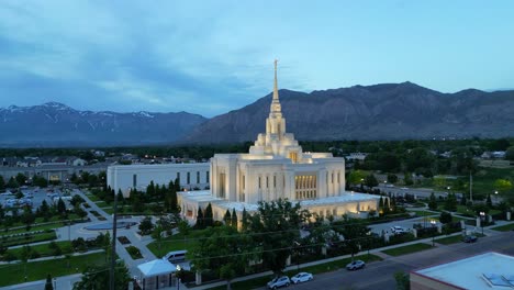 LDS-Mormon-Temple-in-Ogden-Utah-drone-flight-flying-at-dusk-on-beautiful-summer-night-wide-shot-flying-towards-beautiful-religious-temple-building-with-blue-skies-and-mountains-in-background