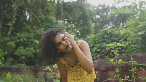 Woman-flips-hair-flirts-with-camera,-wears-yellow-dress-outdoors-forest