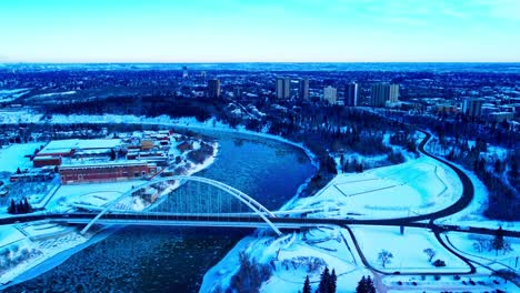 winter aerial forward flyover birds eye view dolly roll over the walter dale tied arch bridge over the north saskatchewan river in between kinsmen park and the rossdale power plant reflective river3-3