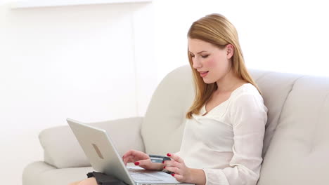 una rubia feliz comprando en línea en el sofá con una computadora portátil