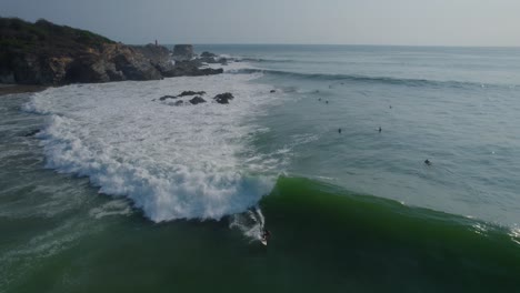 toma aérea de seguimiento de un surfista completando giros acrobáticos y montando una ola