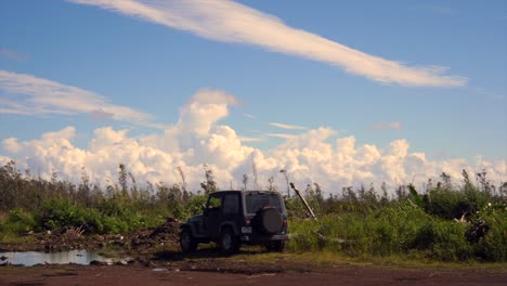 black jeep parked on volcanic land with forest regrowth and impressive cloud formations