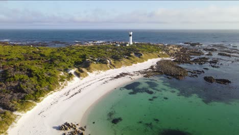 White-lighthouse-and-birds-flying-in-a-protected-bay-in-moonlight-beach,-Pringle-bay