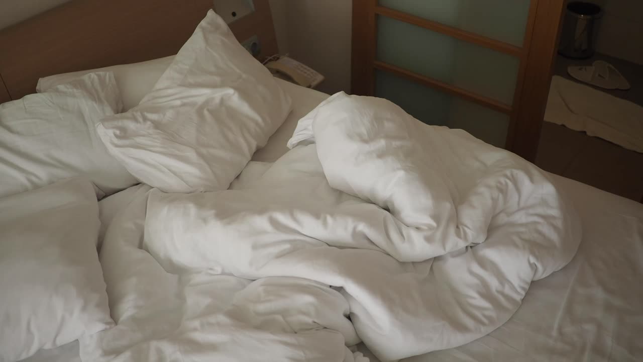 Ranjang yang Belum Dirapikan dengan Seprai Putih dan Bantal di Kamar Hotel