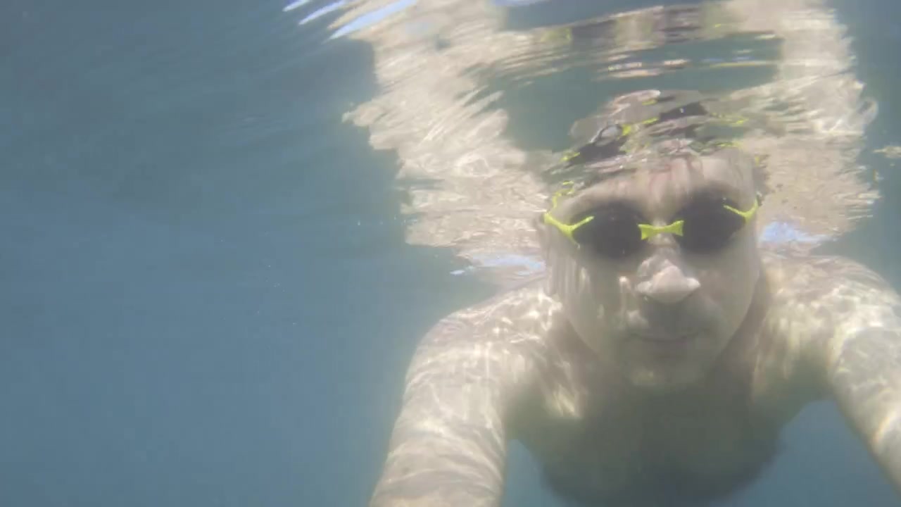 Man actively swimming underwater, holding camera for a selfie. Enjoying vacation leisure and blue ocean water activity