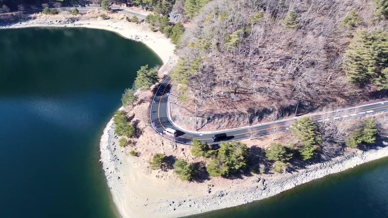 Drone-luftlandskab af to varevogne, der kører ad en naturskøn vej rundt om et sving, omgivet af skovtræer nær Saiko-søen, Fuji-bjerget, Yamanashi, Japan, Asien. Transport og rejse