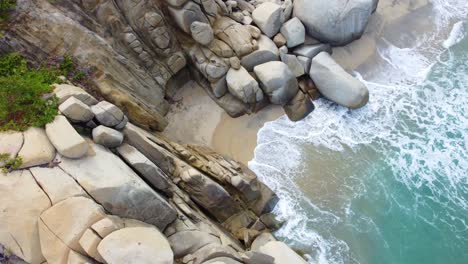 light blue waves crashing against beach lined with large boulders