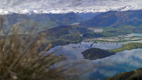 a beautiful green valley with mountains above a lake on a bright sunny day on a grassy hill, drifting handheld shot. new zealand.
