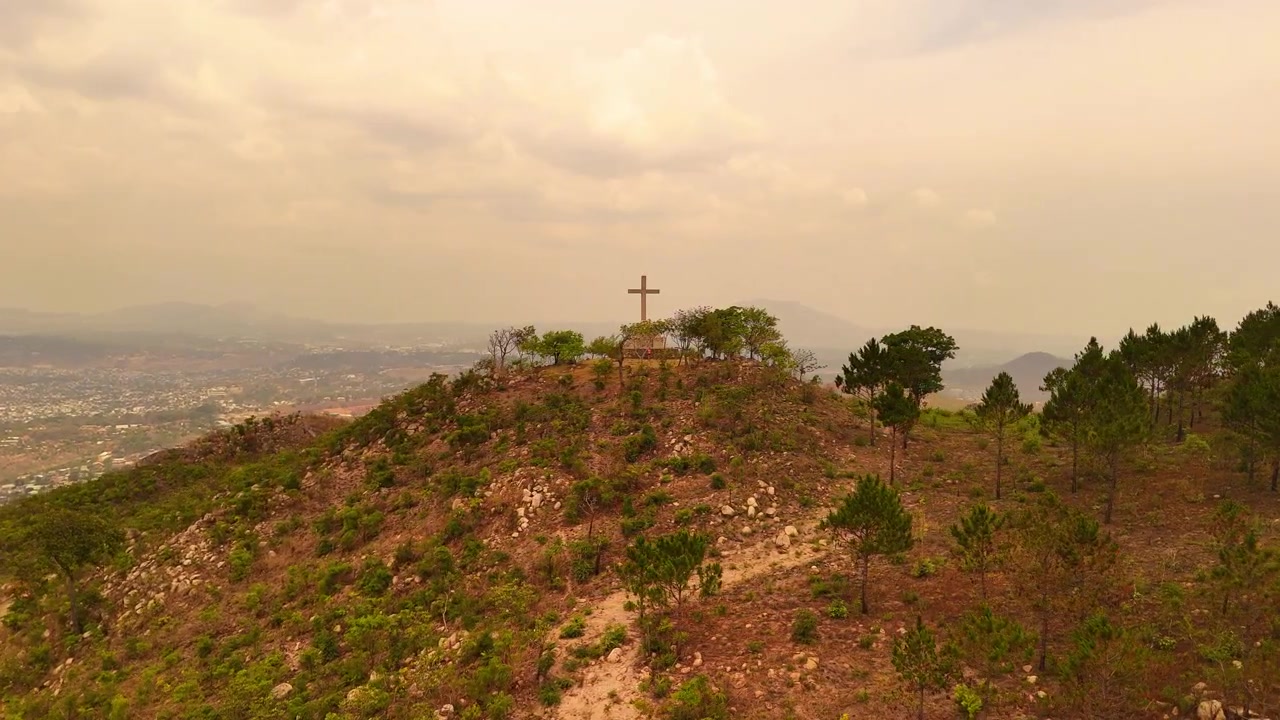 Um sobrevoo circular na Via Sacra da Montanha Michiru, mostrando árvores jovens plantadas e um fraco horizonte de Blantyre sob uma névoa branca.