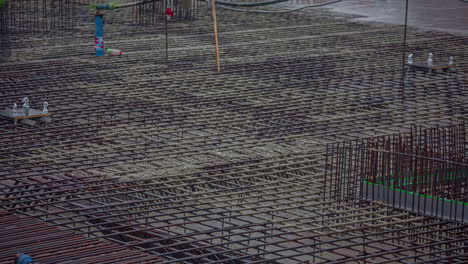 toma general de un gran sitio de construcción con trabajadores vertiendo cemento sobre varillas de acero en un lapso de tiempo durante el día