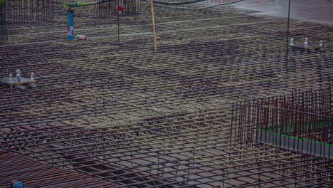 overview shot of big construction site with workers pouring cement over steel rods in timelapse at daytime