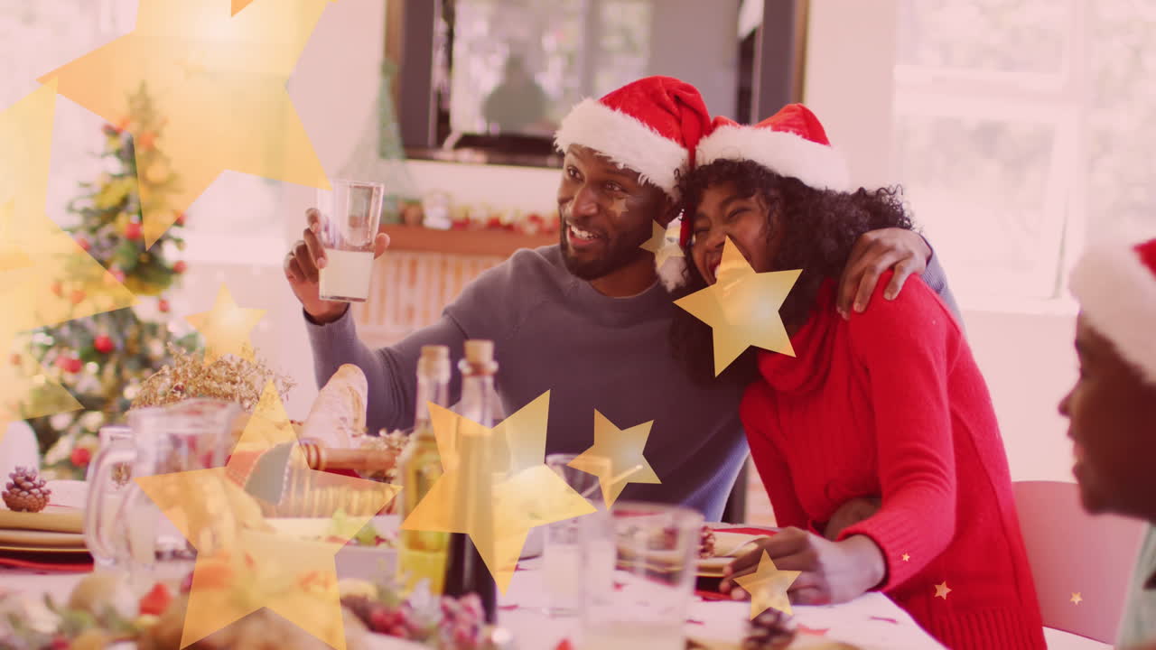 animación de estrellas cayendo sobre una feliz familia afroamericana con sombreros de papá noel y cenando