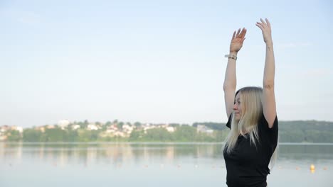 a young woman in a black tshirt against the background of the lake and the sky does yoga a young woman in a black tshirt against the background of the lake and the sky does yoga a woman practices yoga outdoors
