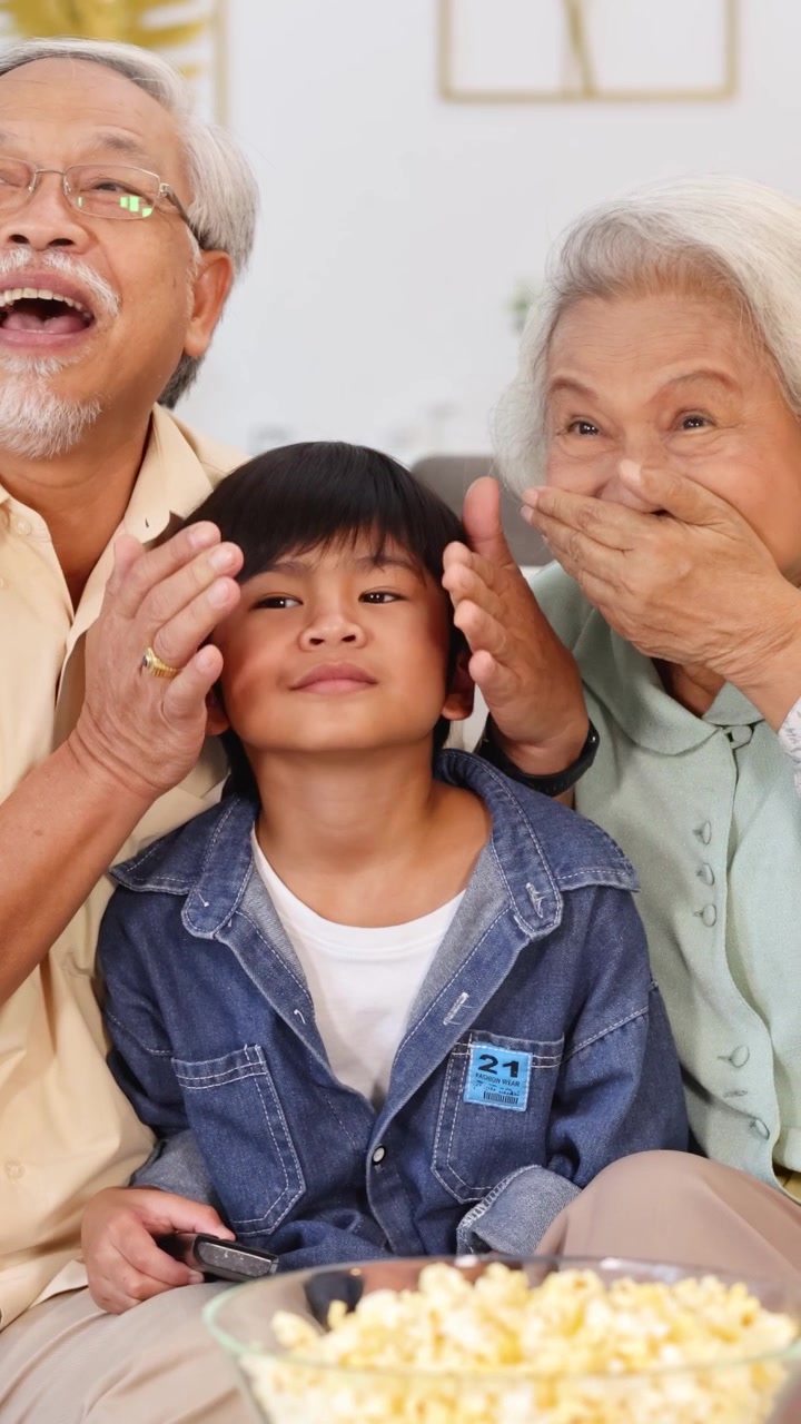 Un gioioso momento in famiglia con i nonni che coprono giocosamente gli occhi di un bambino durante un film a casa