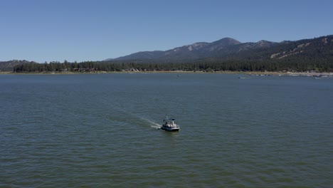 Aerial-drone-tracking-shot-of-a-blue-boat-in-Big-Bear-Lake-in-San-Bernardino-County,-California