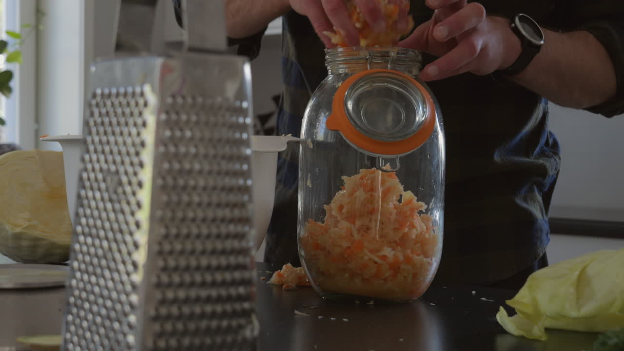 человек насыпает морковно-капустную смесь в стеклянную банку, готовый к процессу брожения напиток комбуча, концепция