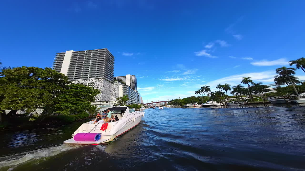 Yachts stand on anchor at the waterfront and sail by the river. FPV drone approaches the moving boat and flies around it.