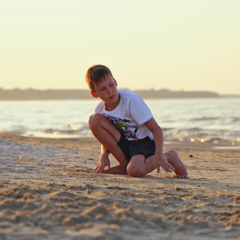 boy plays on sand beach on the sea background in summer. young teenager playing alone with sand on the shore in the evening.