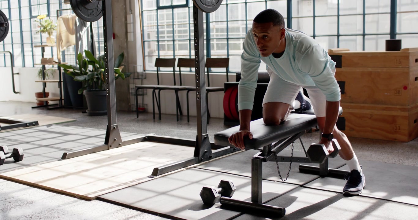African American man reaching for dumbbell and rowing on bench for strength, copy space