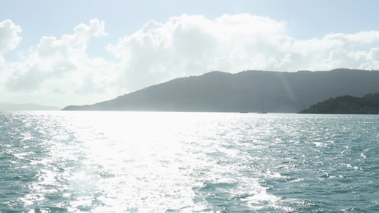 Bright afternoon sun reflecting off the ocean with land in the distance.