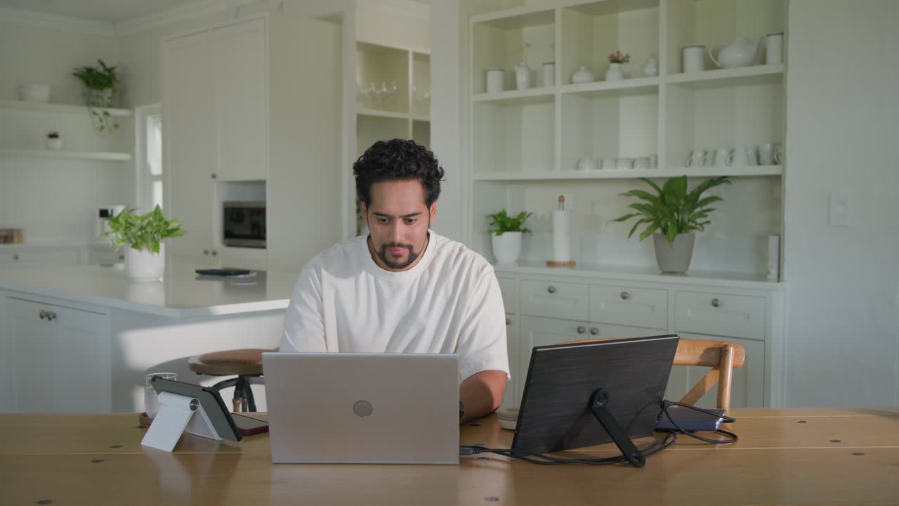 Homem afro-americano sentado em casa, reagindo a um som, digitando no laptop, verificando monitor, trabalhando.
