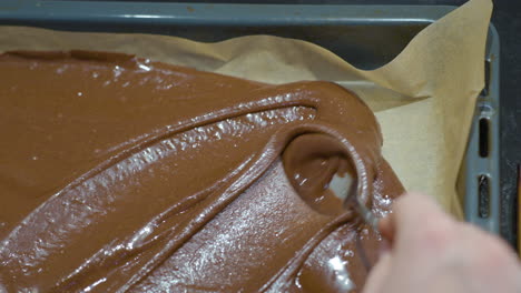 woman's hand spreading brownie dough on baking tray with spoon close-up