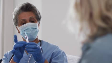médica afroamericana mayor con máscara preparando la vacunación para la mujer en casa