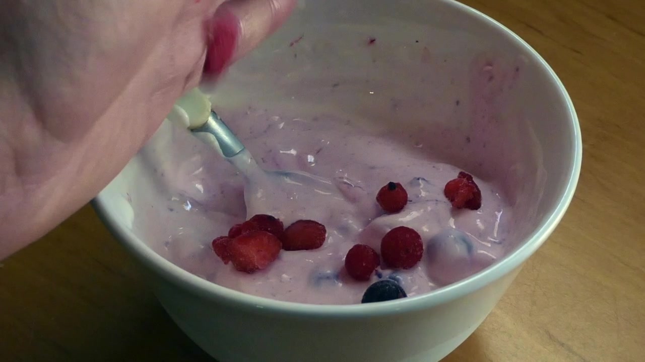 Persona che aggiunge lamponi e mirtilli in una ciotola di yogurt per una colazione sana