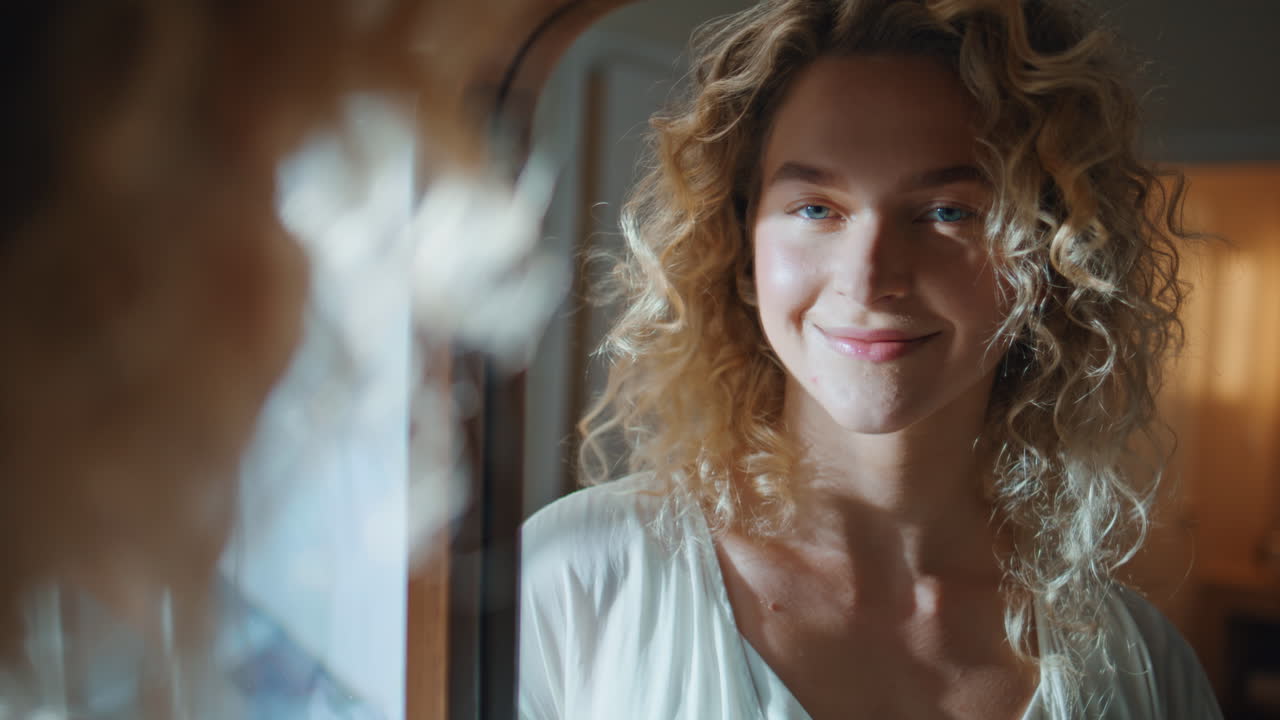 Confident girl looking mirror reflection closeup. Smiling curly woman admiring