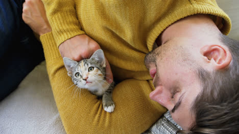 Young-man-lying-on-sofa-stroking-his-pet-cat-while-holding-her-in-his-arms-4K-4k