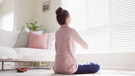 caucasian woman sitting on floor, practicing yoga and meditating in living room