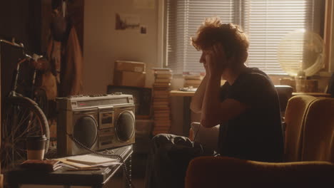 young man in headphones relaxing at home, enjoying music on boombox