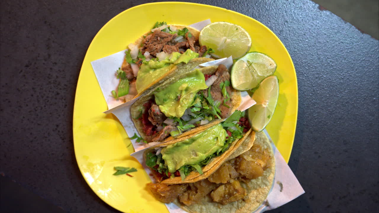 Slow motion overhead shot of a yellow plastic plate with a variety of tacos at a traditional mexican restaurant