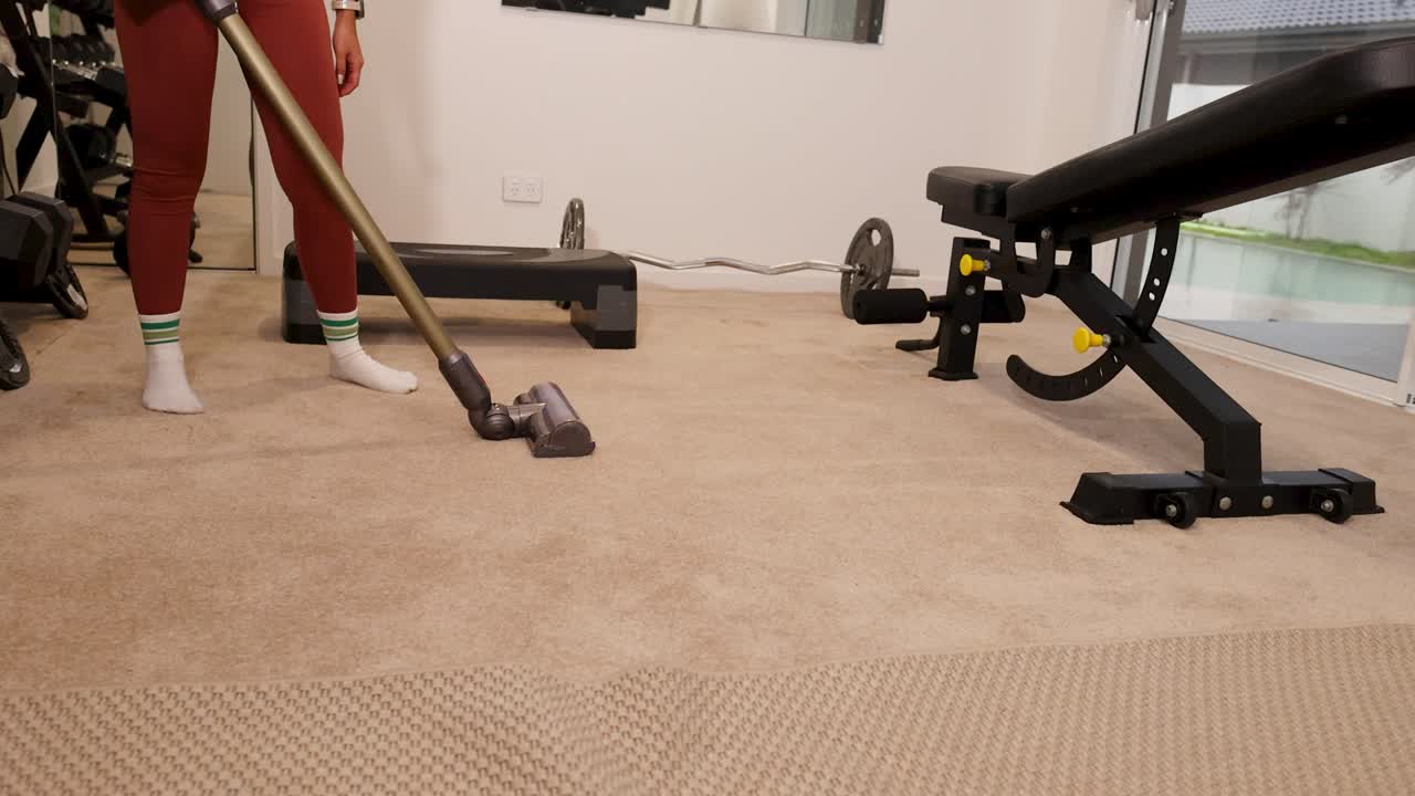 A person vacuums a gym carpet in a well-lit fitness room, focusing on cleanliness and maintenance