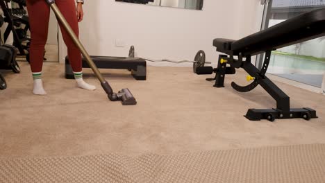 a person vacuums a gym carpet in a well-lit fitness room, focusing on cleanliness and maintenance