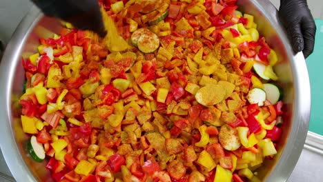 close-up from above of a chef sprinkling curry spice over chopped vegetables in a large pot in slow motion